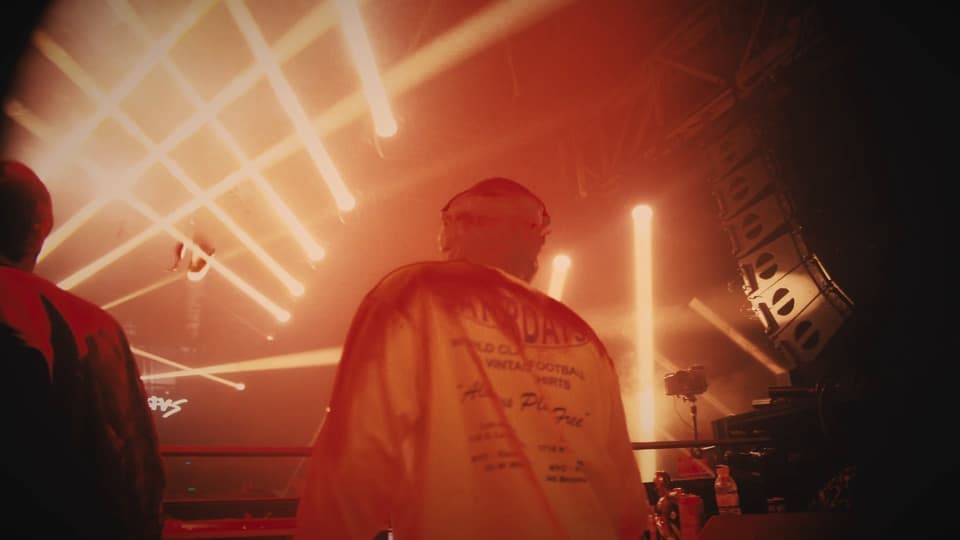Un DJ de espaldas entre los haces naranjas, en The Bow